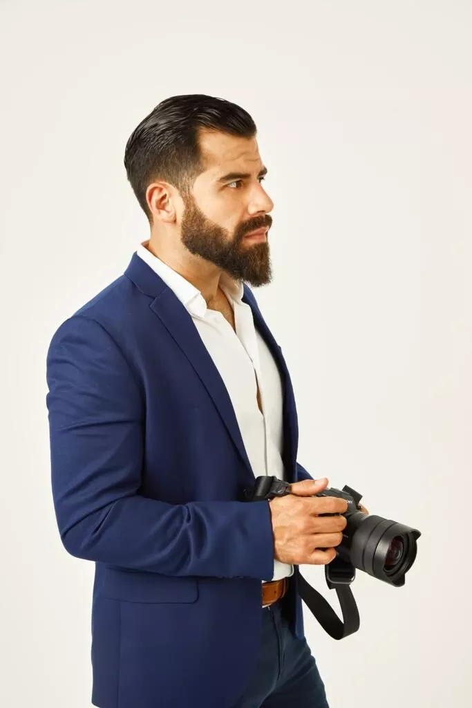 Jorge Alvarez in a navy blazer holding a mirrorless camera against a white background