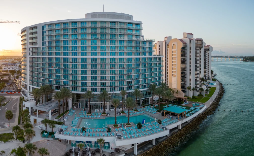 Aerial view at sunset of the Opal Sands hotel pool deck and curved glass facade by the water