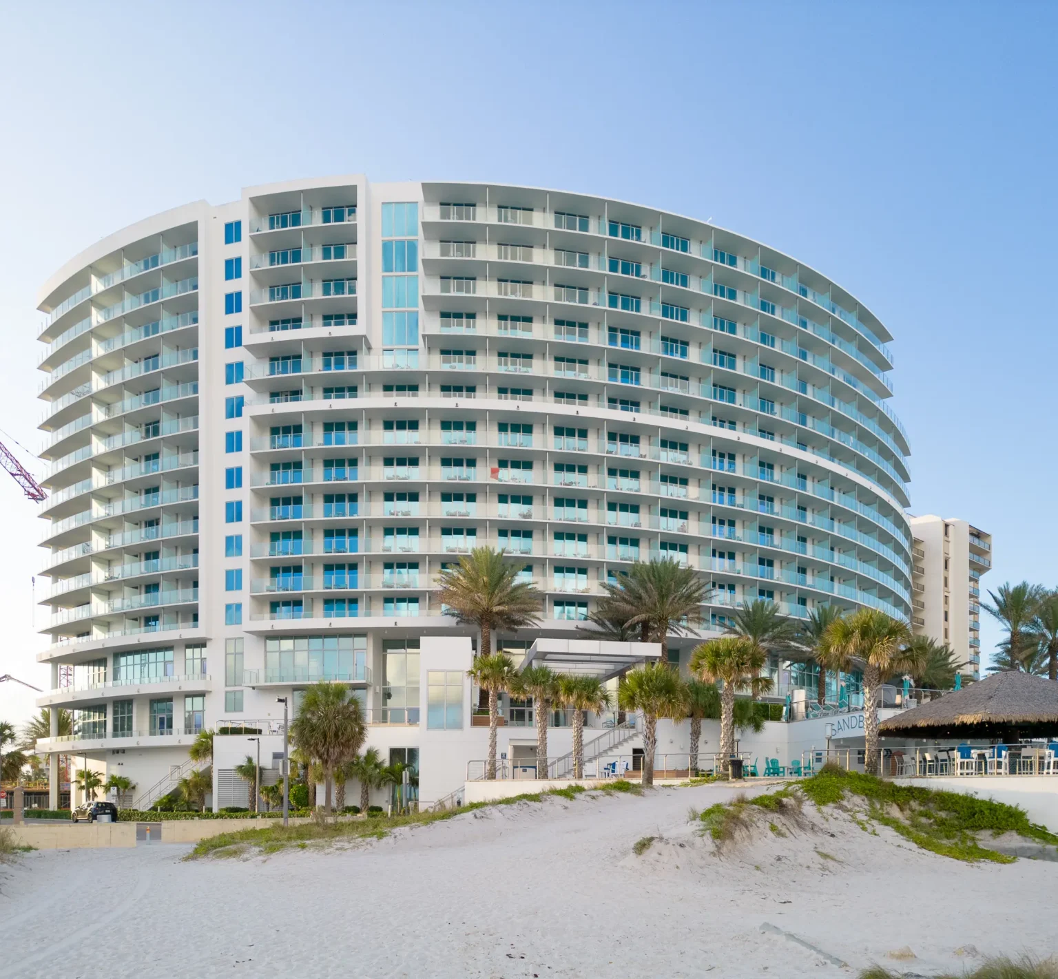 Curved glass facade of Opal Sands Resort rising above white sand and palm trees on Clearwater Beach