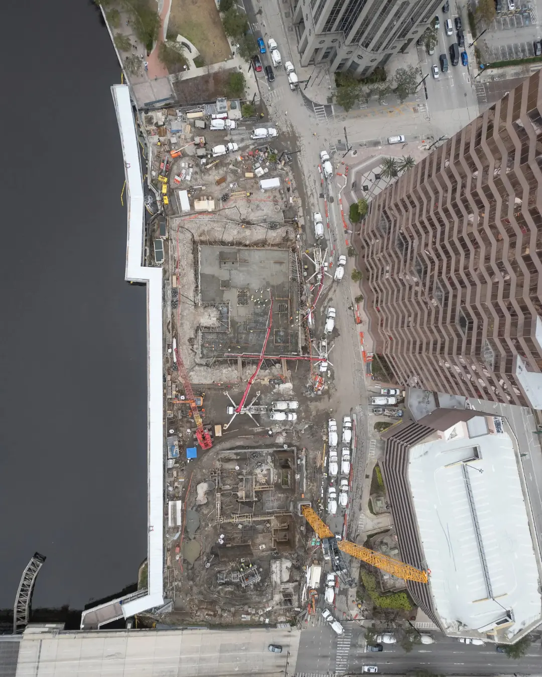 Top-down drone view of a waterfront construction site with cranes, trucks, and material staging areas, by Drone Permission