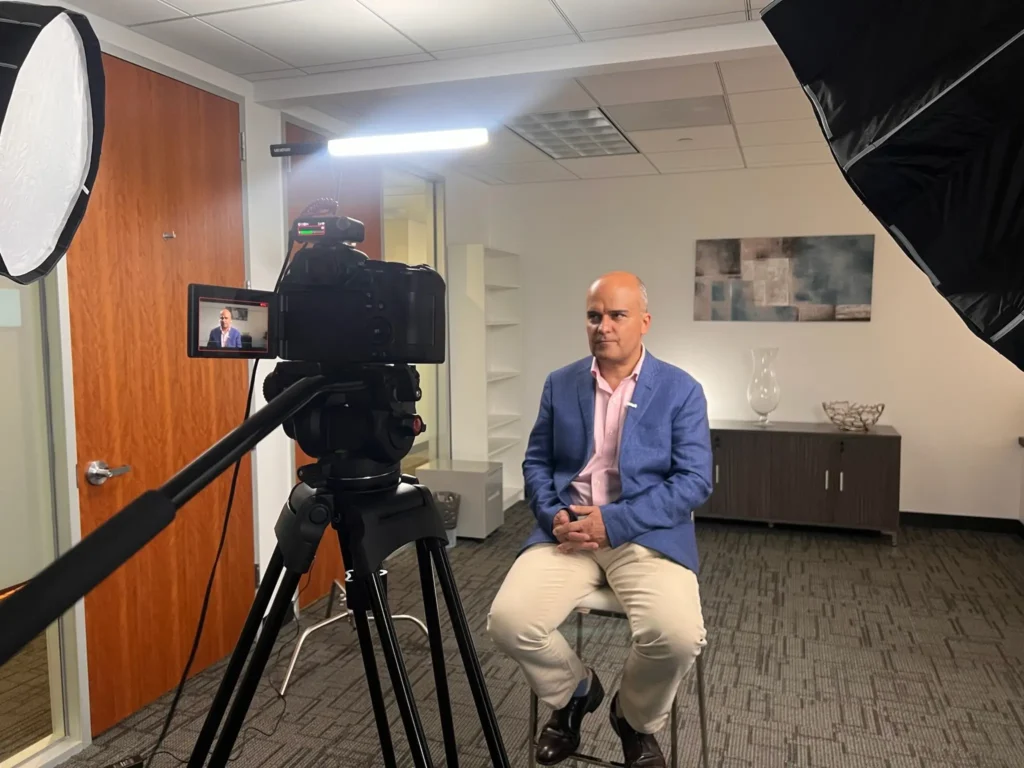 Behind the scenes of a video interview setup with a camera, softbox lighting, and a seated businessman, by Drone Permission