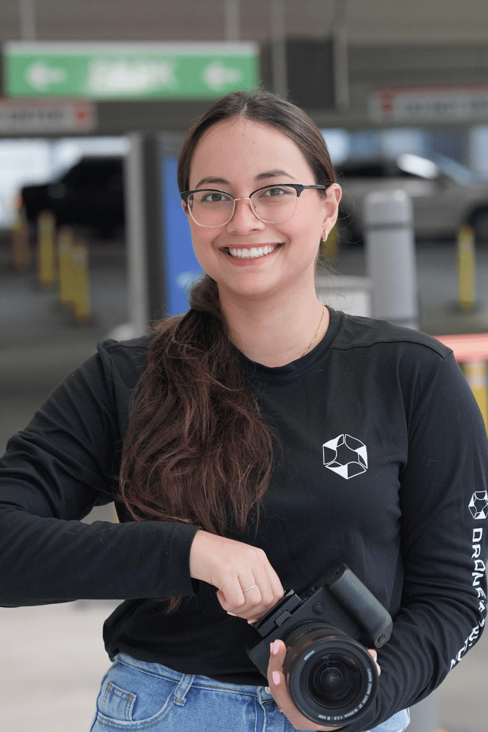 Manuela Delgado, Professional Videographer at Drone Permission, smiling and holding a camera in a parking garage