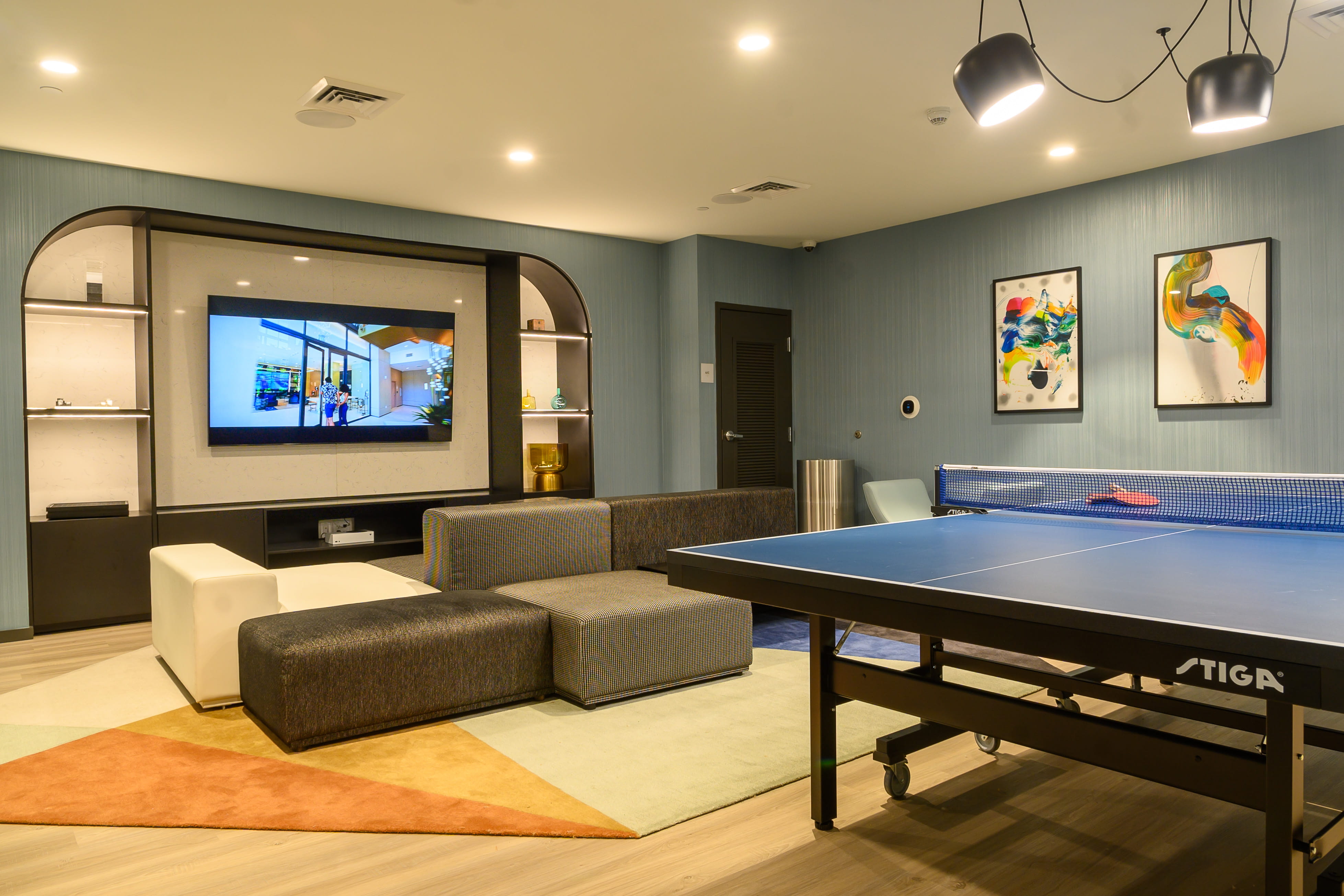 Residents game room with blue ping pong table, sectional sofa and large wall TV at the Slate project