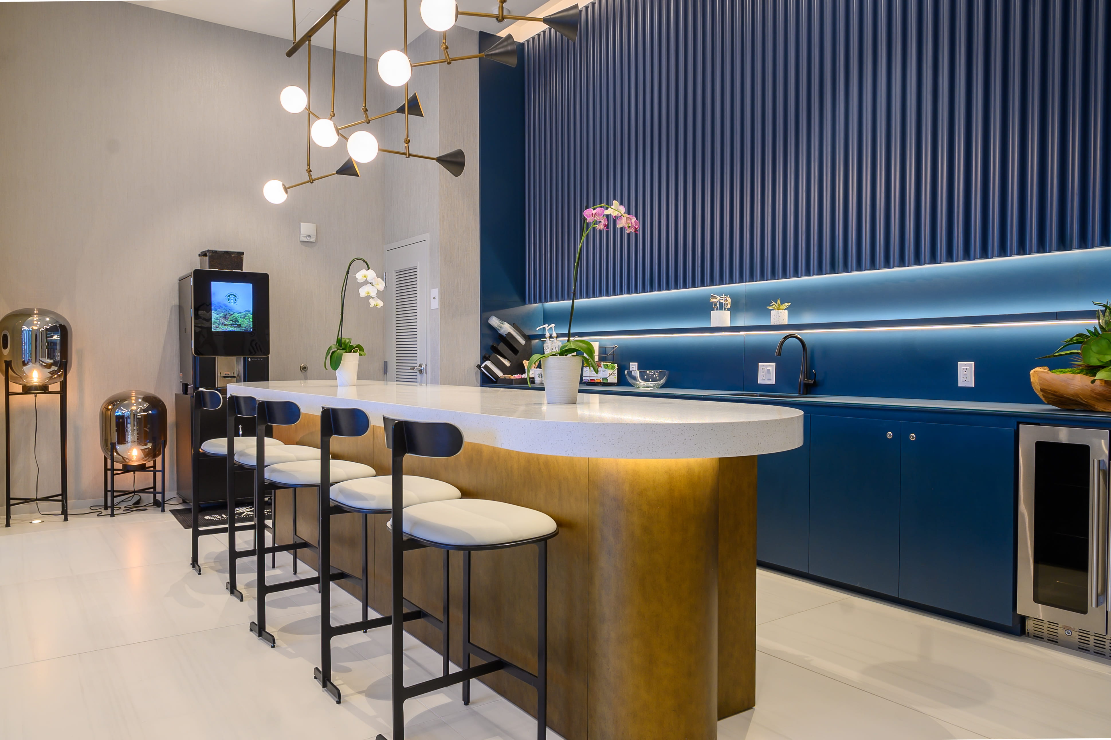 Modern amenity lounge kitchen with white stone island bar, stools and blue fluted wall paneling