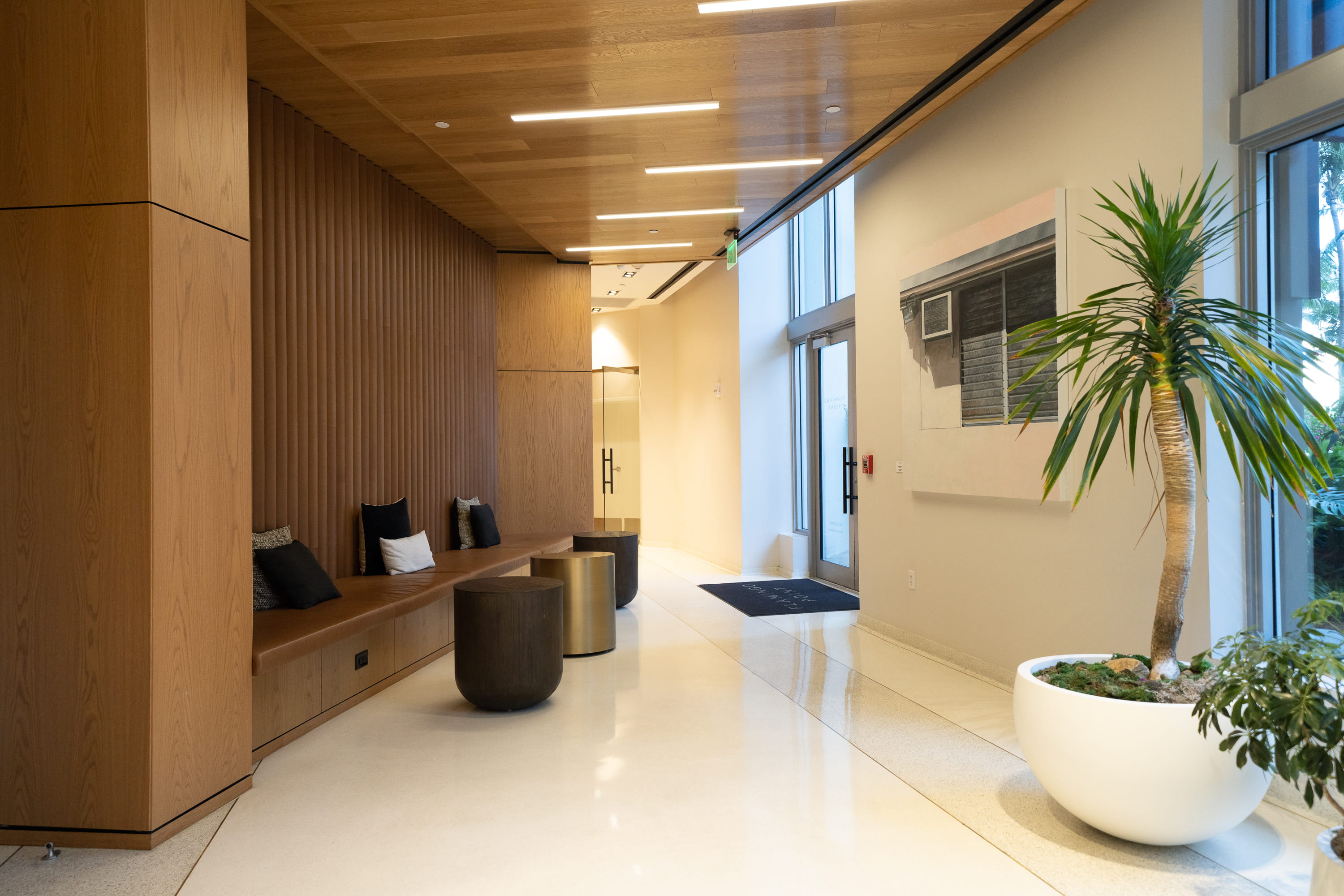 Graded interior frame of the wood paneled lobby with bench seating and a potted palm at the Flamingo residential building