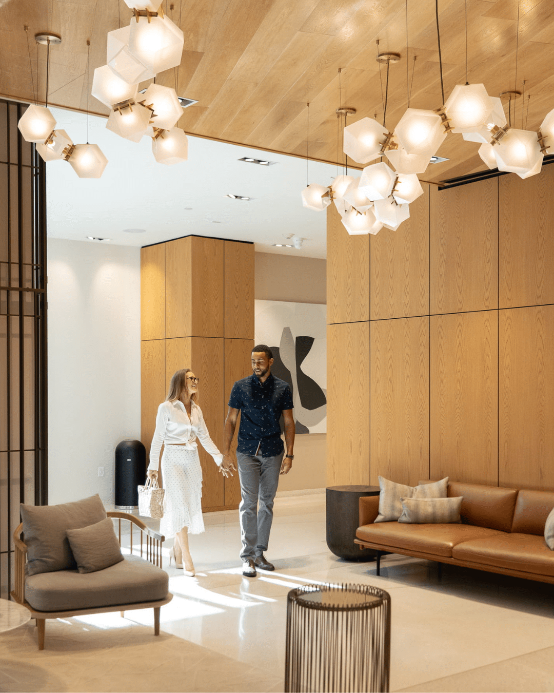 Couple walking through a modern residential lobby with wood paneling and sculptural glass chandeliers