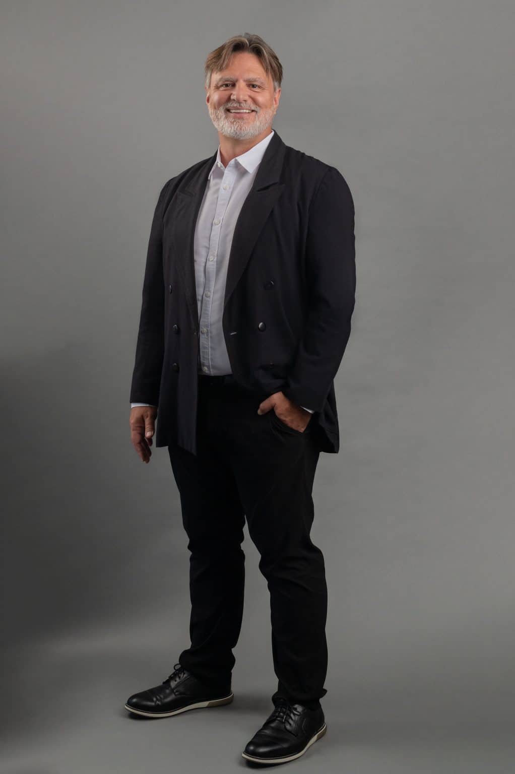 Studio portrait of a man in a dark blazer and jeans against a gray backdrop