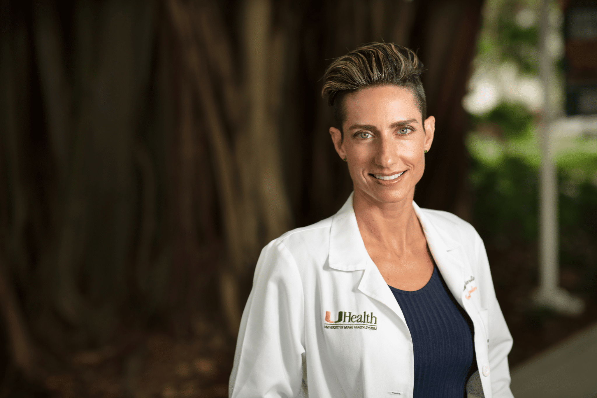 Smiling physician with short hair in a white UHealth coat, outdoor corporate headshot in Miami