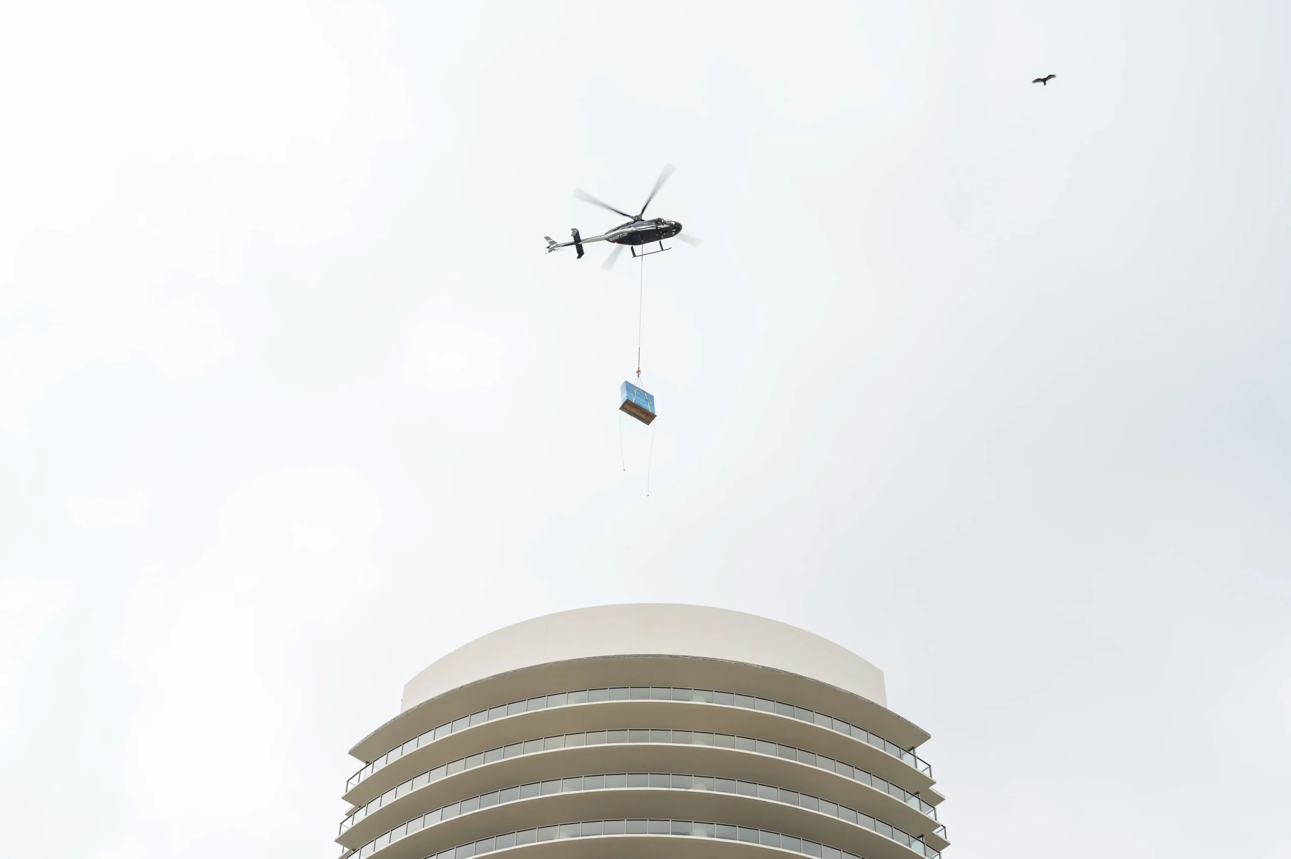 Helicopter carrying a load on a long line above the crown of the St. Regis Residences under construction