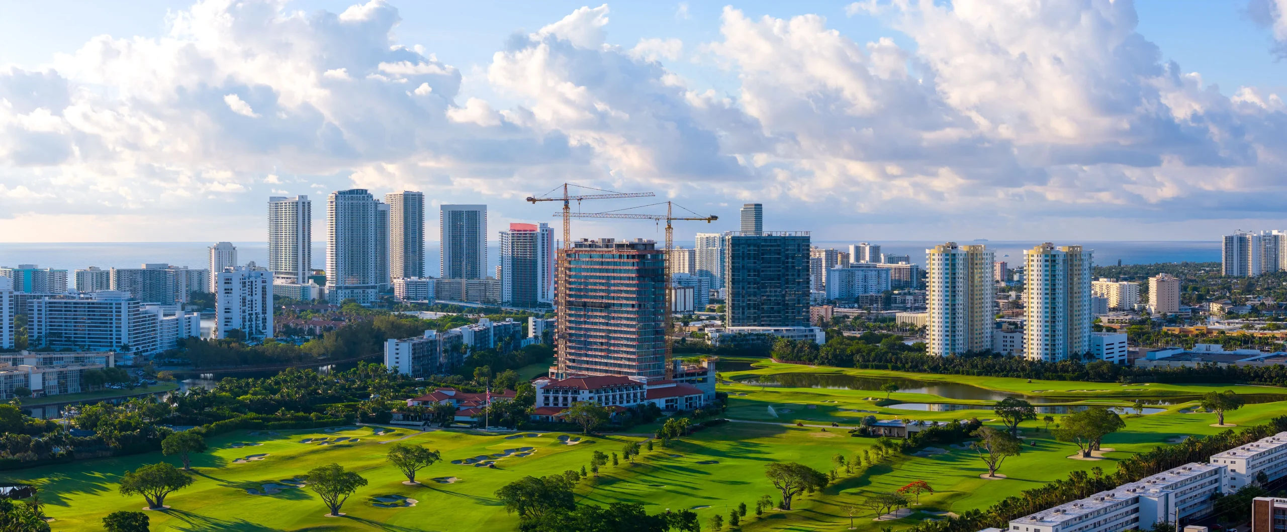Wide aerial of the Shell Bay golf course with Tower 200 under construction in the center and the Hallandale Beach skyline behind, by Drone Permission