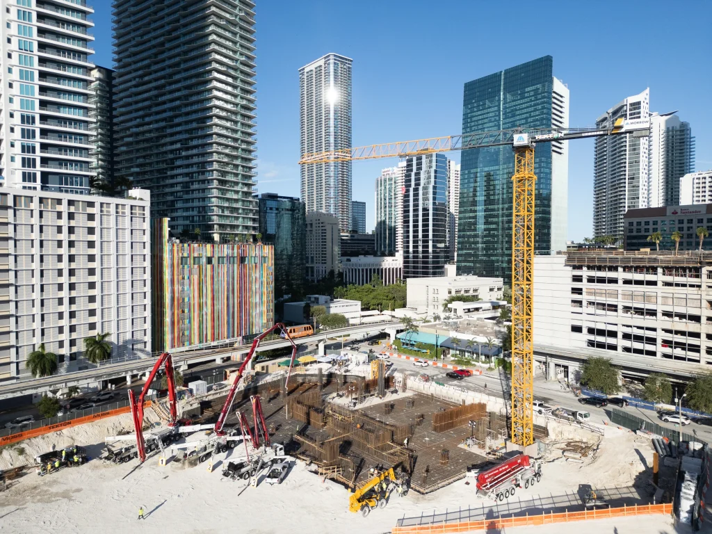Aerial view of the Cipriani Residences Miami foundation pour with red concrete boom pumps, a tower crane, and Brickell high-rises in the background