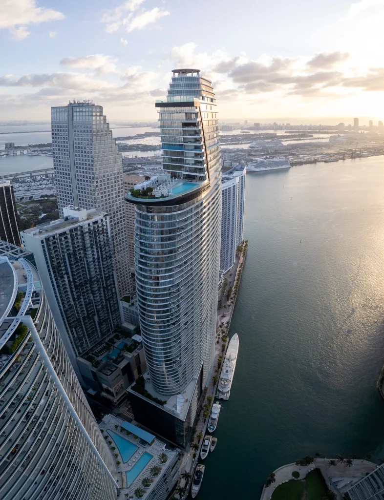 Vertical aerial of Aston Martin Residences and its rooftop pool deck overlooking Biscayne Bay and PortMiami at sunrise, with yachts docked below