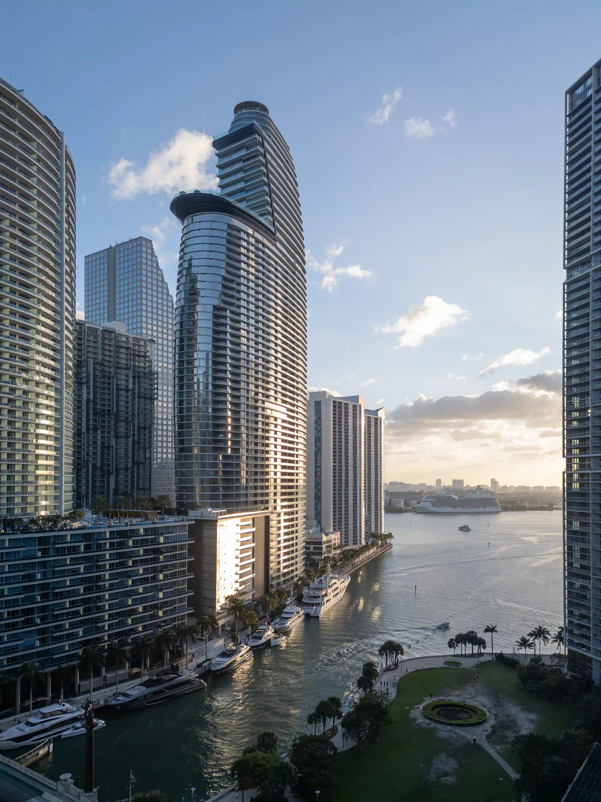 Aerial drone photo at sunrise of Aston Martin Residences on the Miami River with Brickell towers, superyachts and Biscayne Bay in the background