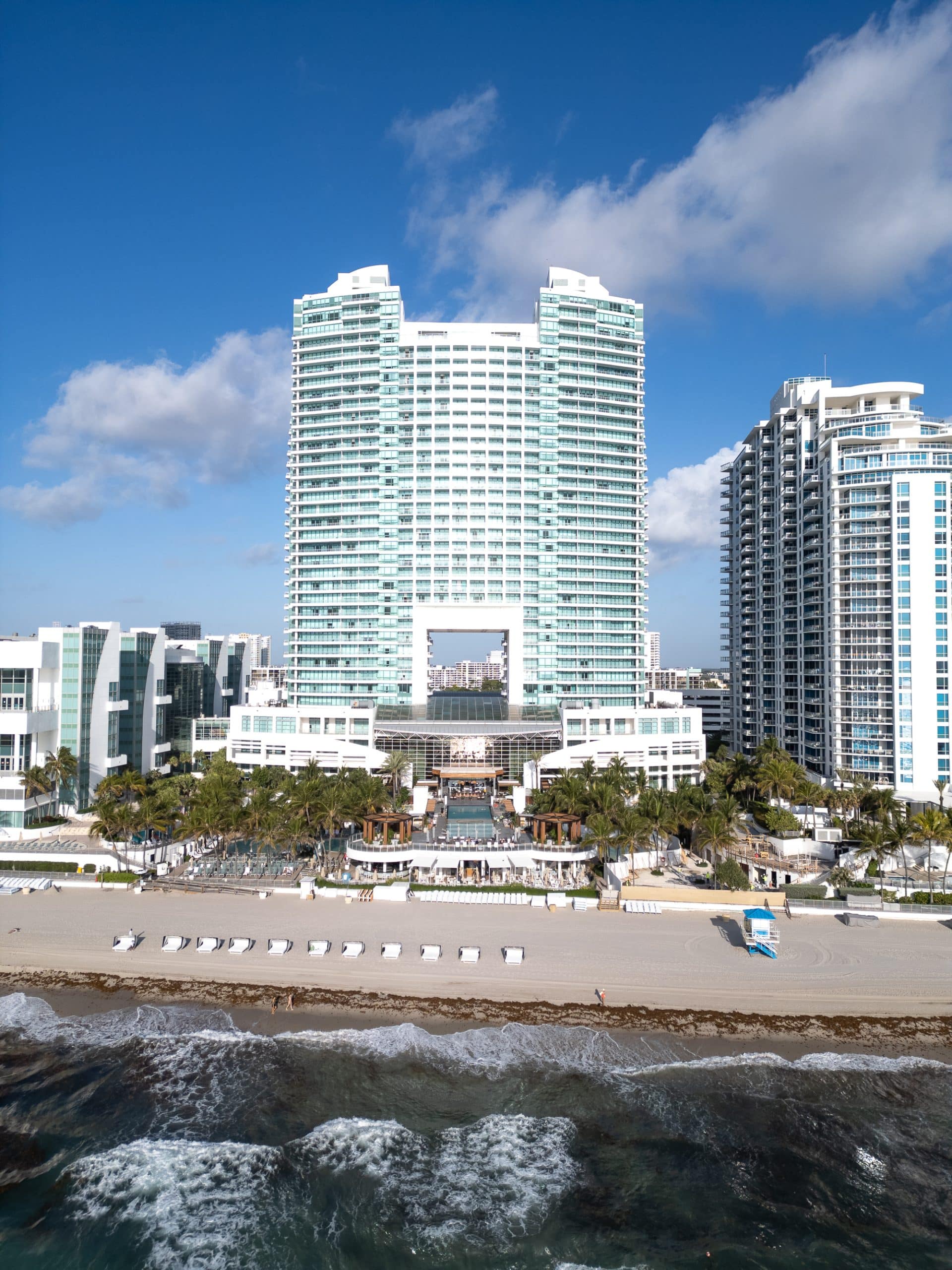 Aerial photo from over the ocean of The Diplomat Beach Resort in Hollywood, Florida, showing the twin-arch tower, pool deck, palm trees and beachfront