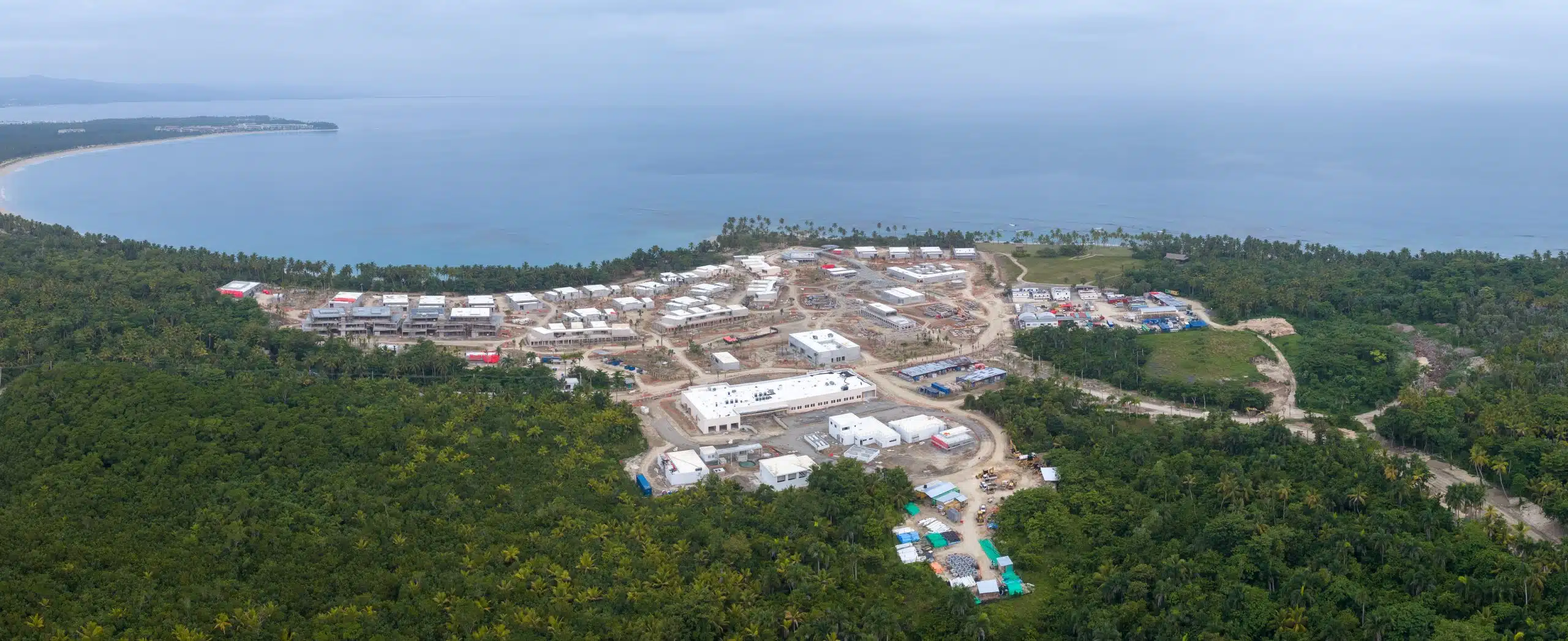 Panoramic aerial view of the Tropicalia beachfront resort construction site in June 2026, showing completed building shells and roofing across the oceanfront development