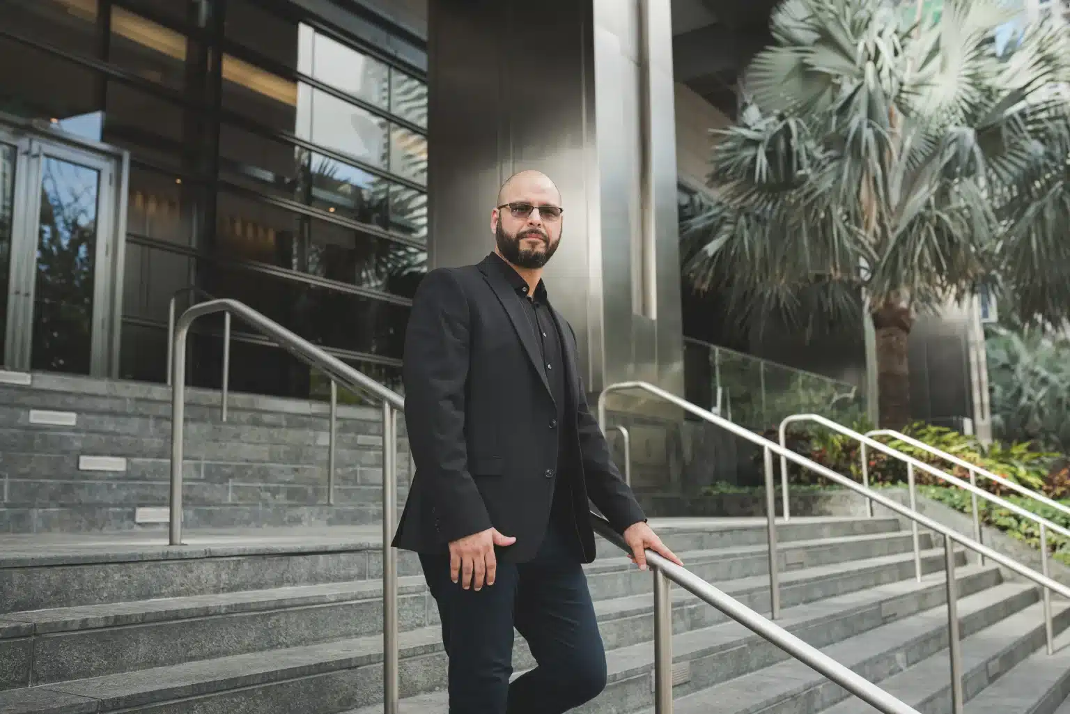 Environmental corporate headshot of a man in a black blazer on the entrance steps of a Brickell high-rise in Miami