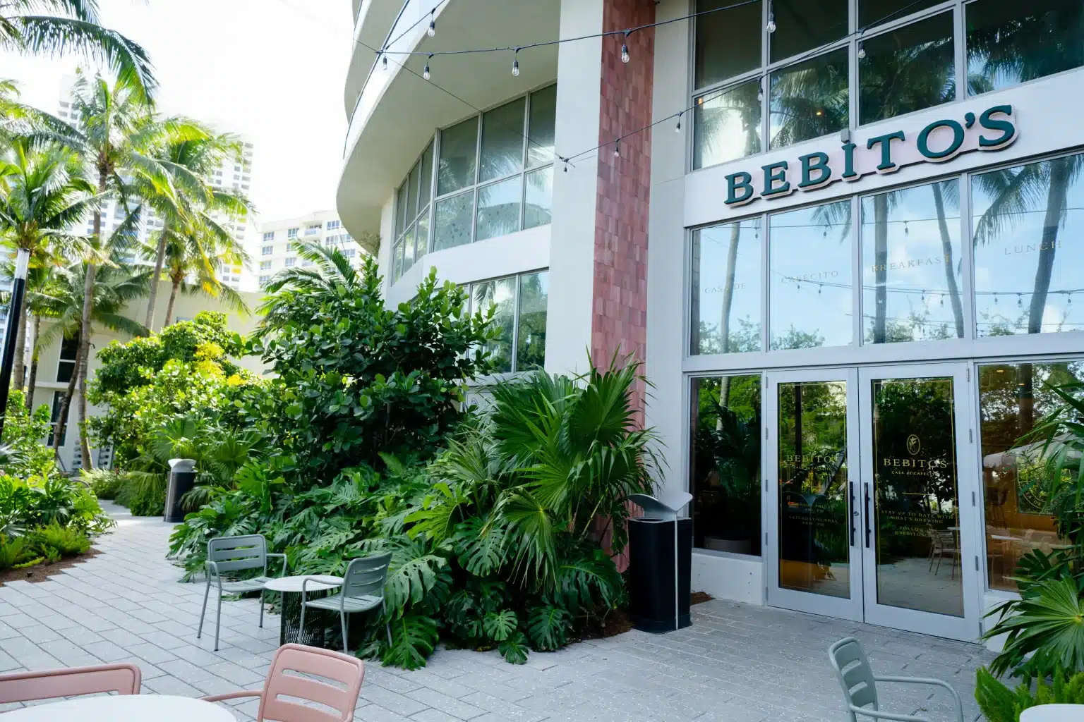 Restaurant entrance with glass doors, outdoor seating and tropical landscaping at Flamingo Point in Miami Beach