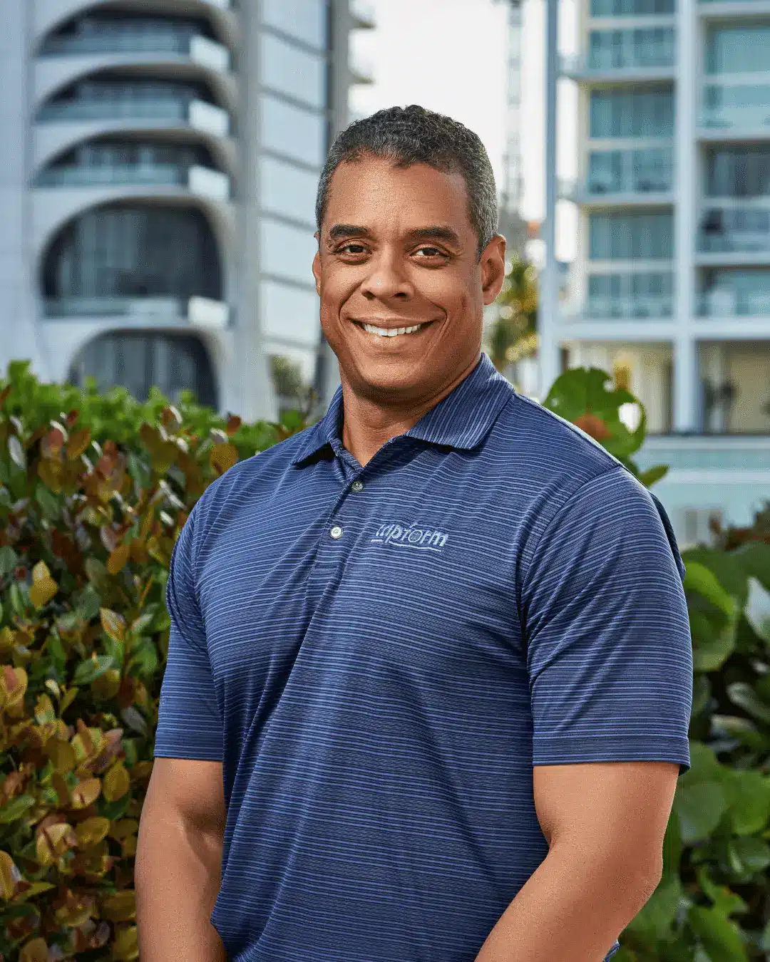 Outdoor corporate headshot of a smiling man in a navy polo in front of high-rise towers in Miami